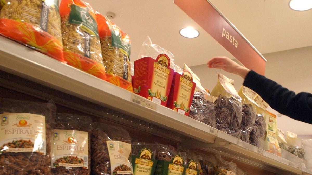 Una mujer coge un paquete de pasta en un supermercado.