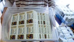 Una mujer lleva en una caja decenas de décimos de la Lotería de Navidad 2022 en una administración de Barcelona.
