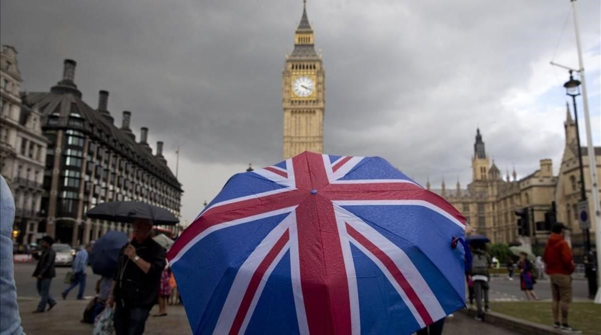 Un transeúnte se refugia de la lluvia en un paraguas con la bandera británica, cerca del Big Ben. Un transeúnte se refugia de la lluvia en un paraguas con la bandera británica, cerca del Big Ben.