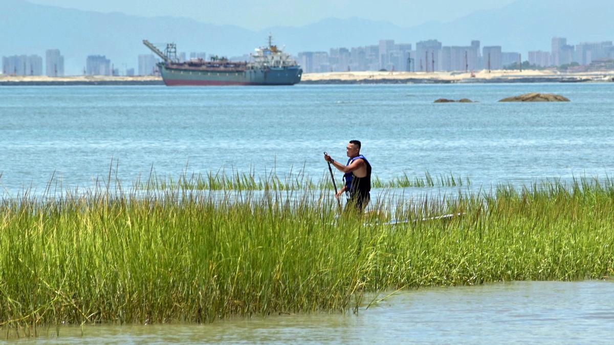 Un hombre rema entre juncos mientras se ve el horizonte de la ciudad de Xiamen  desde las islas Kinmen de Taiwán, que se encuentran a solo 3,2 km de la costa de China continental