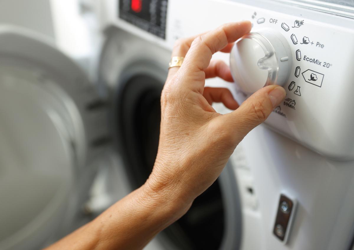 Una persona programando una lavadora. 