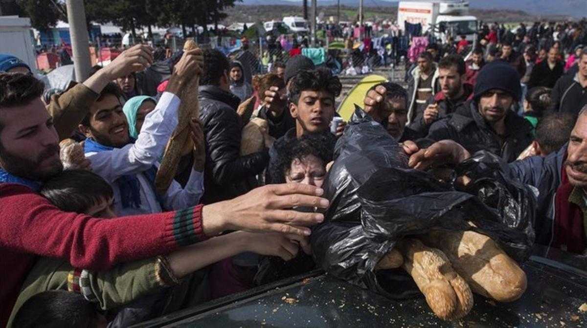 Refugiados que intentan entrar en Macedonia intentan hacerse con pan que reparte una voluntaria en el campo de refugiados cerca de Idomeni.
