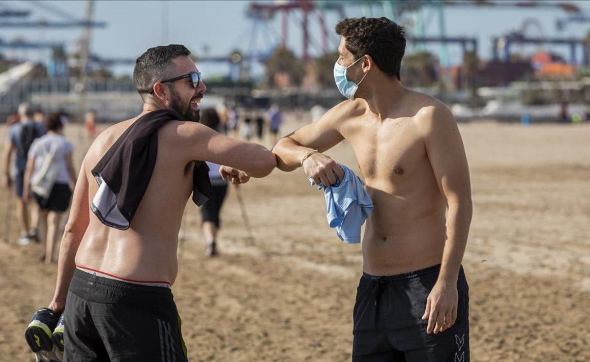 Dos jóvenes se saludan con el codo en la playa de Valencia. Dos jóvenes se saludan con el codo en la playa de Valencia.