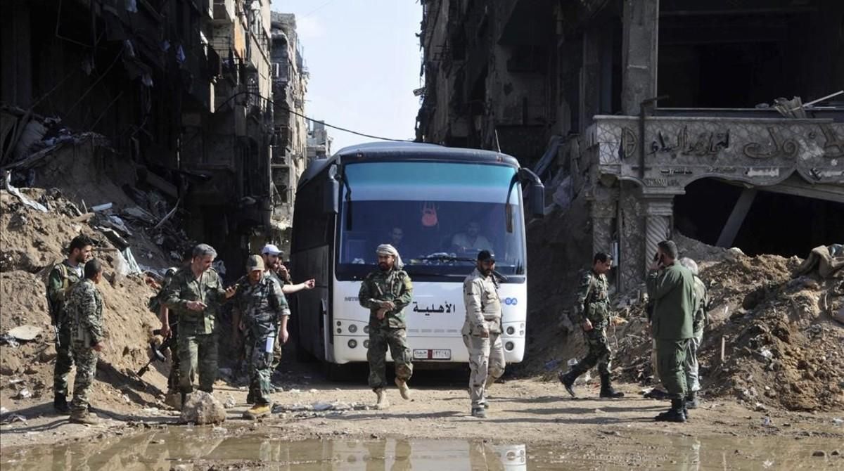 Militares del Ejército sirio supervisan un autobús que transporta combatientes vinculados a Al Qaeda durante una evacuación desde el campo de refugiados palestinos de Yarmuk, cerca de Damasco. Militares del Ejército sirio supervisan un autobús que transporta combatientes vinculados a Al Qaeda durante una evacuación desde el campo de refugiados palestinos de Yarmuk, cerca de Damasco.