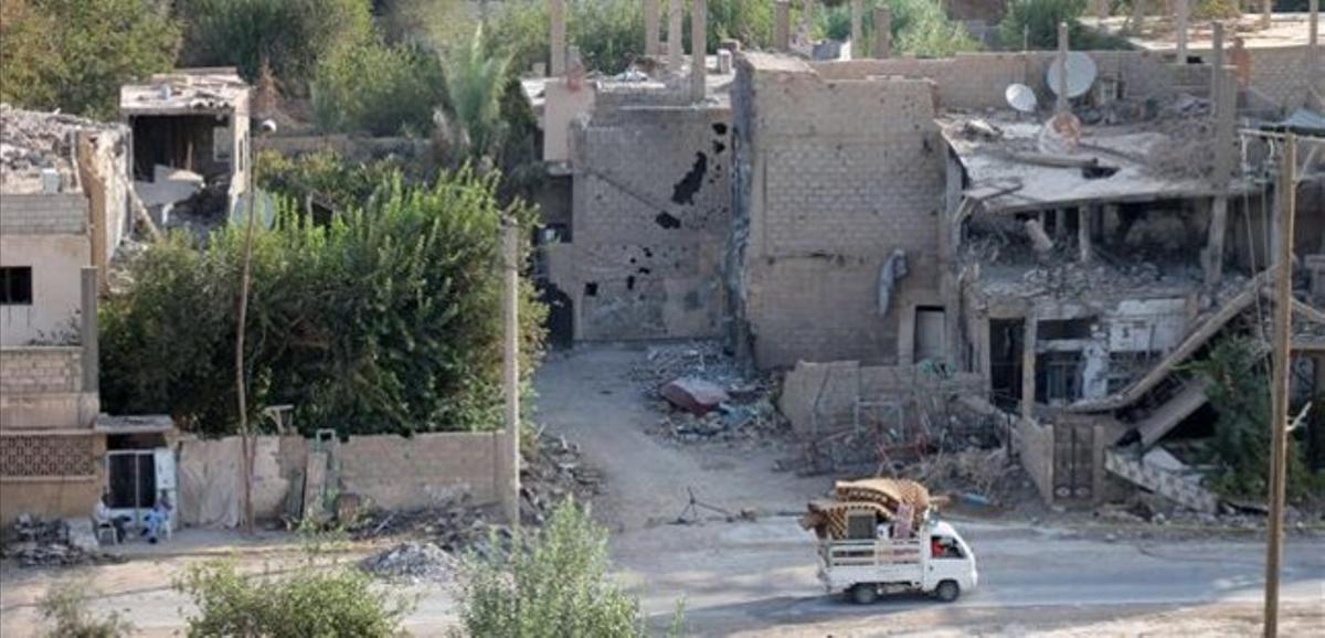 Una ’pick-up’ circula junto a edificios destruidos en Deir Ezzor, en el este de Siria, este lunes.