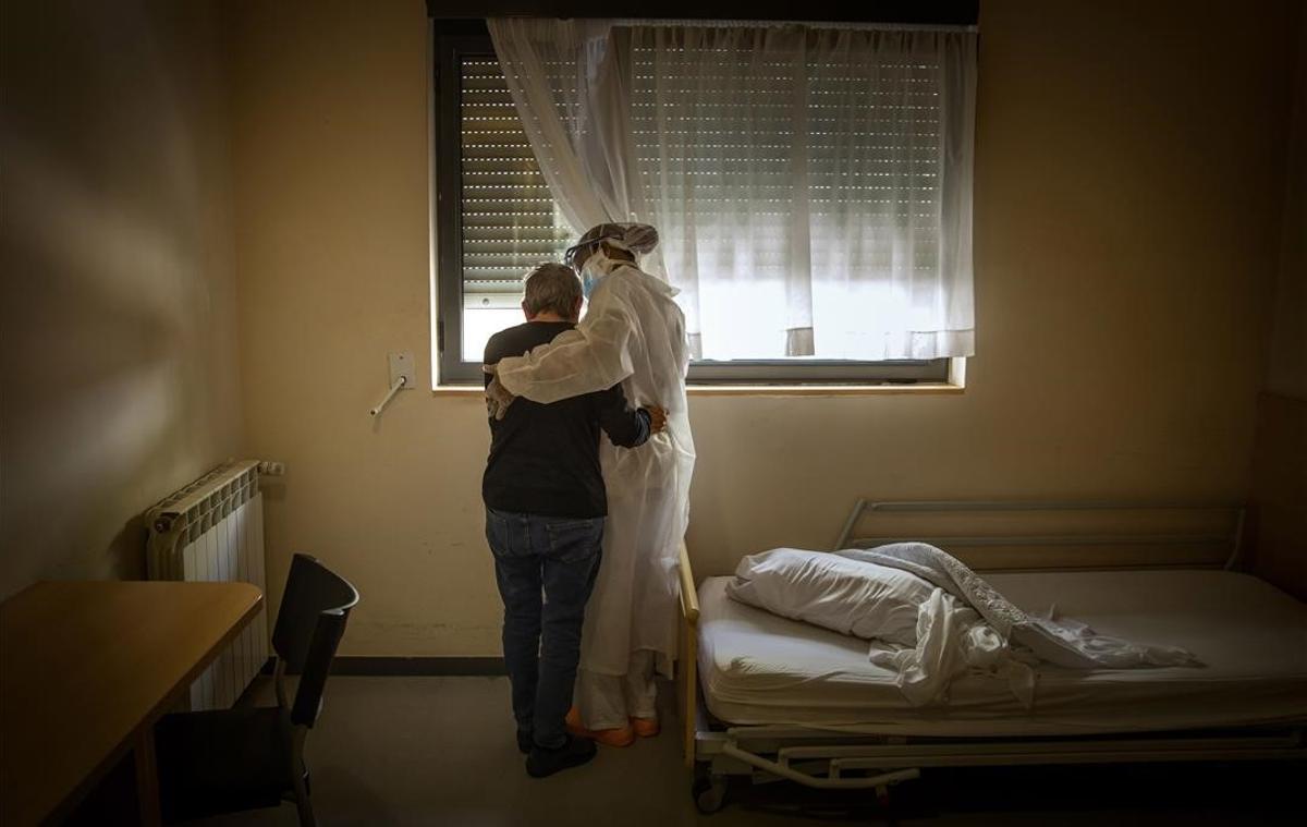Una anciana y una trabajadora se abrazan en la habitación en la que la primera permanece confinada, en una residencia de la provincia de Barcelona.