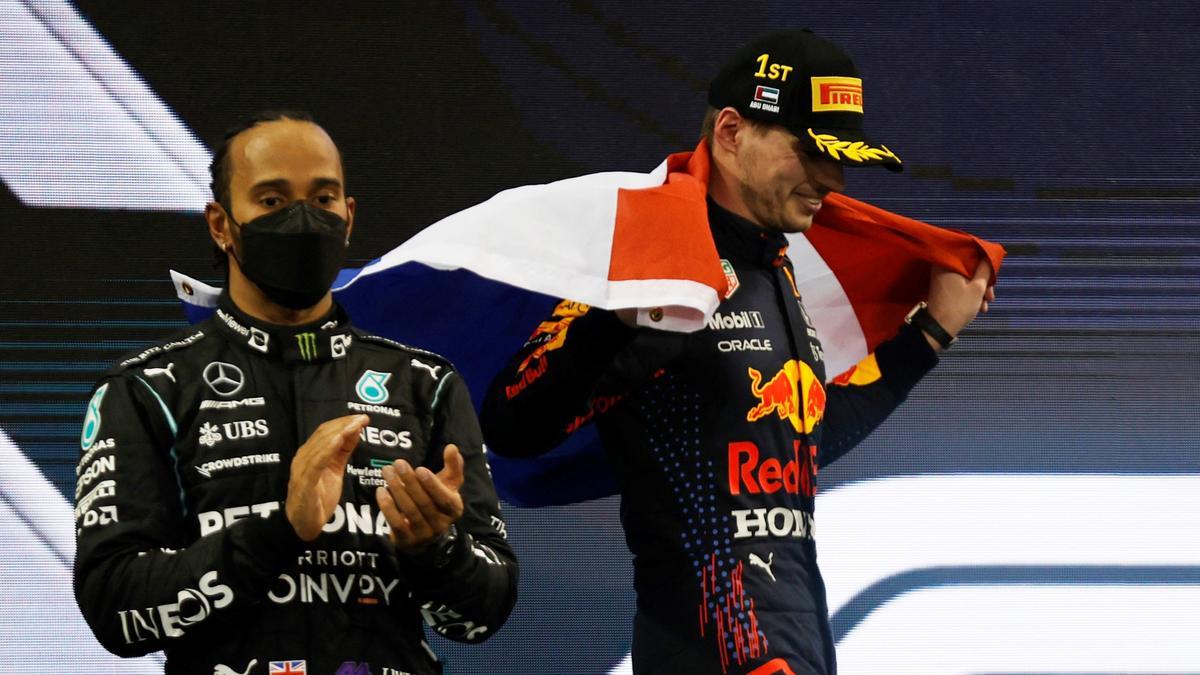 Max Verstappen de Red Bull celebra ganar la carrera y el campeonato mundial con la bandera de los Países Bajos en el podio, mientras Lewis Hamilton, de Mercedes, observa después de terminar en segundo puesto.