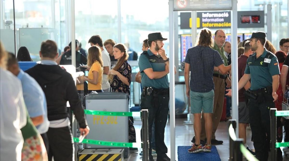 Un usuario pasa bajo el arco de detección de metales de la T-1 del aeropuerto de El Prat ante la mirada de dos guardias civiles. 