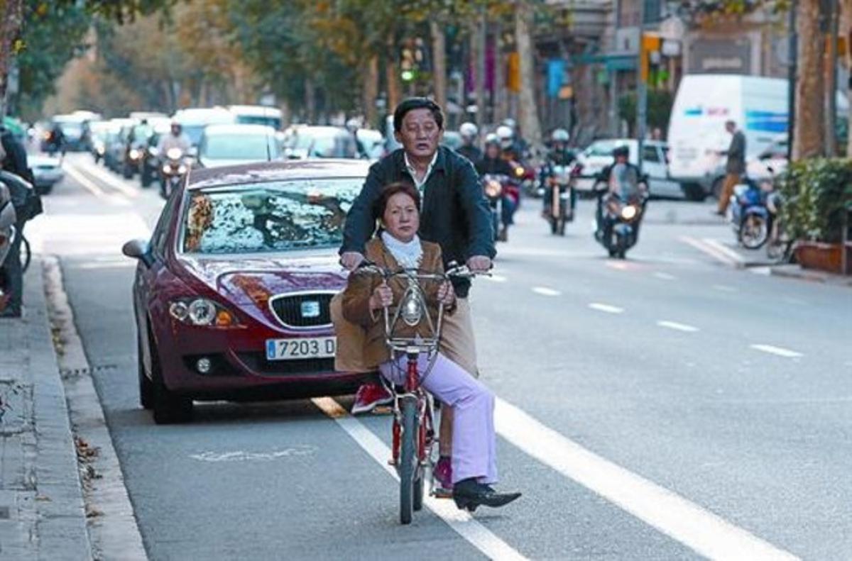 Una pareja de ciudadanos chinos circula en una bici del Bicing por la calle Consell de Cent después de sortear un coche parado en su carril, ayer.
